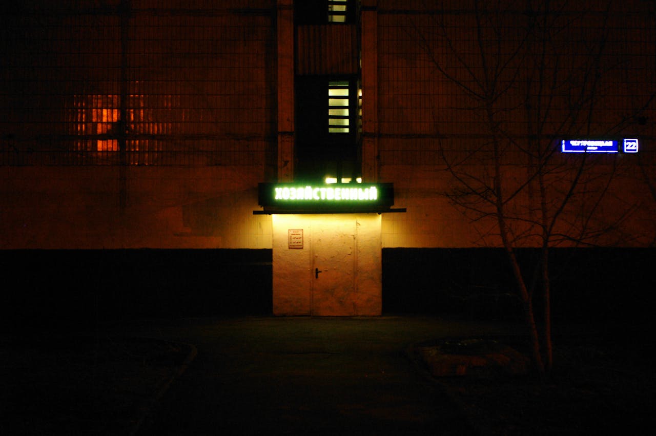 A dark urban scene illuminated by a neon sign, creating a moody atmosphere.